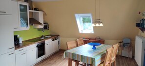 Cocina compacta con armarios blancos, microondas y un pequeño comedor con mesa y sillas.