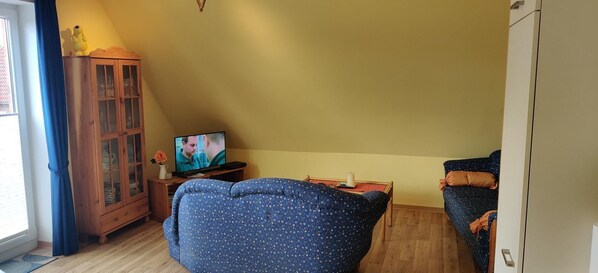 Una sala de estar con un sofá azul, un aparador de madera y un televisor sobre un mueble bajo.