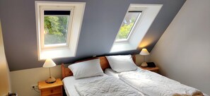 A bedroom with a bed, two bedside lamps, a nightstand, and two skylights.
