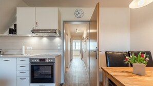 Una cocina moderna con armarios blancos, horno integrado y comedor con mesa y sillas de madera.