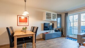 Una sala de estar moderna con una mesa de comedor de madera, sillas negras, un televisor y un mueble gris.