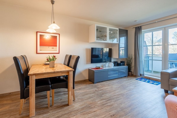 A modern living room with a wooden dining table, black chairs, a TV, and a grey cabinet.