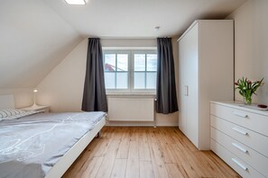 A bedroom with a bed, a nightstand, a dresser, a radiator, and a window with curtains.