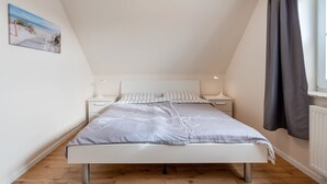 Un dormitorio con cama, mesitas de noche, ventana con cortinas y un cuadro en la pared.
