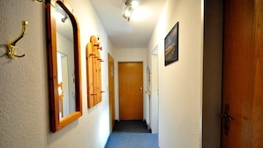Um corredor estreito com uma porta de madeira no fim, um cabide e um quadro na parede.