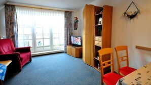 Uma sala de estar com um sofá vermelho, uma televisão, um armário de madeira e uma mesa de jantar com cadeiras vermelhas.