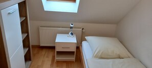 Un dormitorio pequeño y ordenado con una cama individual, una mesita de noche con lámpara, un radiador y una ventana.