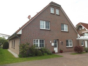 Une maison à deux étages, construite en briques, avec un toit en pente, de nombreuses fenêtres et une antenne parabolique.