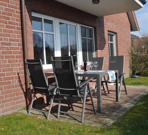 An outdoor patio with a table and chairs, a brick wall, and a window.
