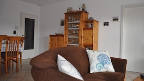 Una sala de estar con un sofá marrón, un mueble de madera con cristalería, y un comedor con una mesa y sillas.