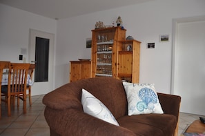 Ein Wohnzimmer mit einem braunen Sofa, einem Holzschrank mit Gläsern und einem Essbereich mit Tisch und Stühlen.