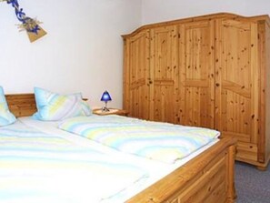 A bedroom with a large wooden wardrobe, a bed with striped bedding, and a nightstand with a lamp.