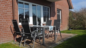 Un patio al aire libre con una mesa, sillas, un ventanal y un muro de ladrillo.