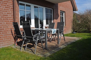 Eine Terrasse im Freien mit Tisch, Stühlen, einem Fenster und einer Ziegelwand.