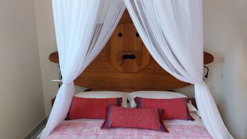 Ein Bett mit Holz-Kopfteil, weißem Baldachin und Bettwäsche in Rot und Pink.