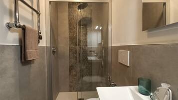 Un bagno moderno con doccia vetrata, lavandino bianco e porta asciugamani.