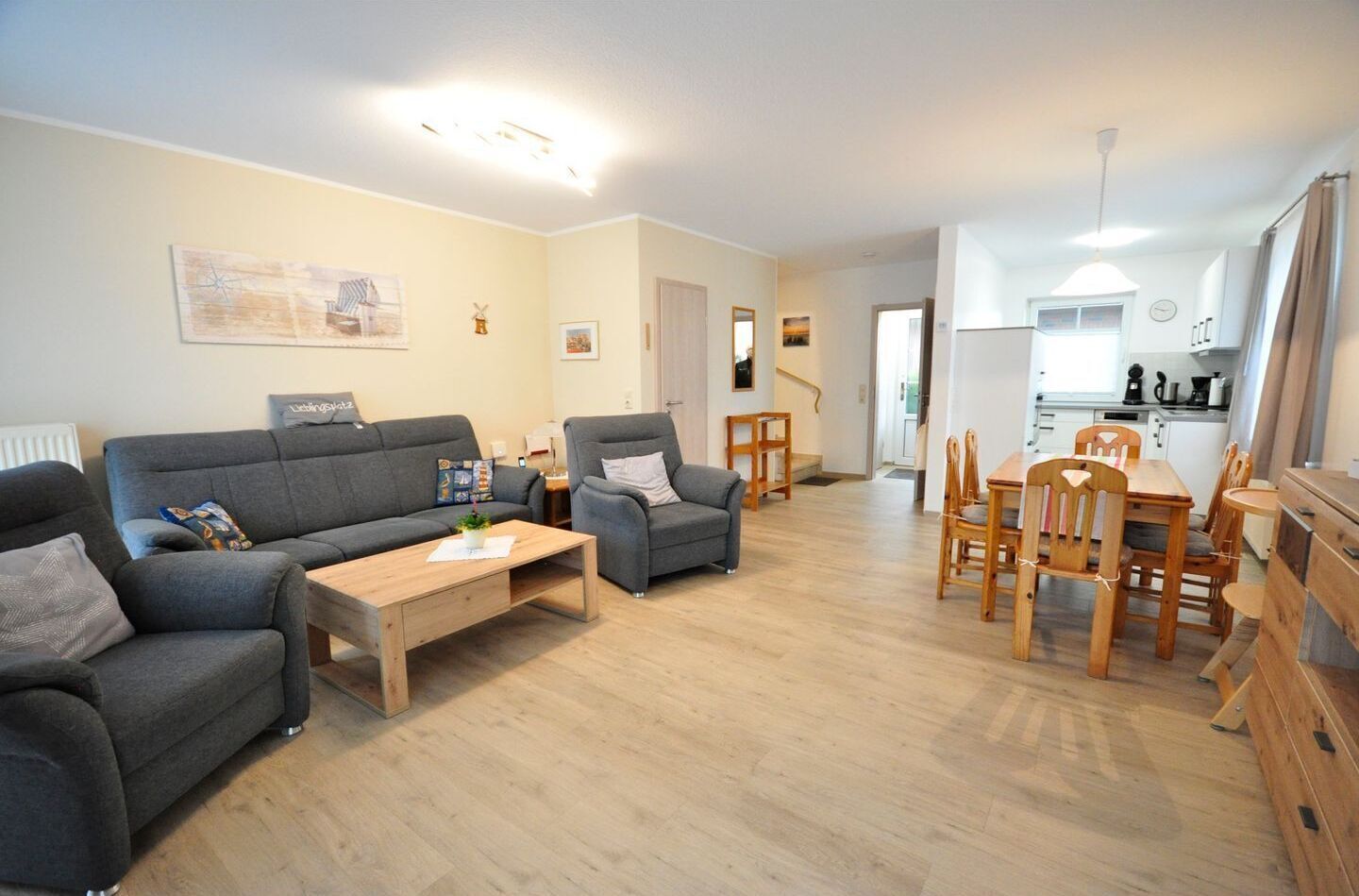 Una sala de estar moderna con un sofá gris, una mesa de centro de madera y un comedor con sillas y mesa de madera.