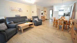 A modern living room with a grey sofa set, a wooden coffee table, and a dining area with wooden chairs and a table. - Terraced house Am Haustierpark House 11 M - Am Haustierpark (Werdum)
