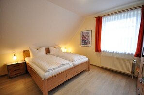 Un dormitorio con una cama de madera, dos mesitas de noche, un radiador y una ventana con cortinas.