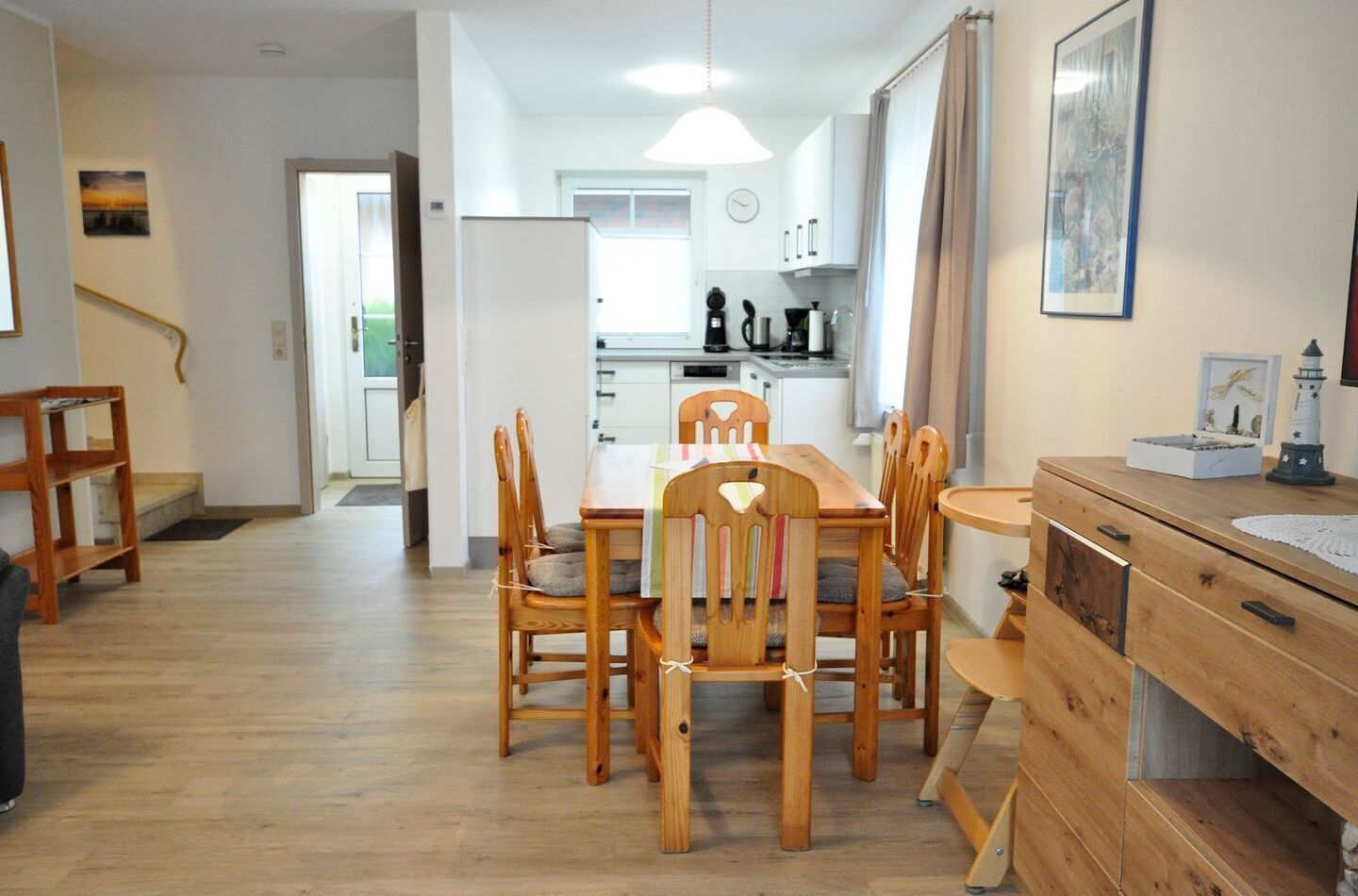 Una cocina moderna con armarios blancos, una mesa de comedor con sillas de madera y una pequeña isla con un lavaplatos.