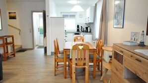 A modern kitchen with white cabinets, a dining table with wooden chairs, and a small island with a sink. - Terraced house Am Haustierpark House 11 M - Am Haustierpark (Werdum)