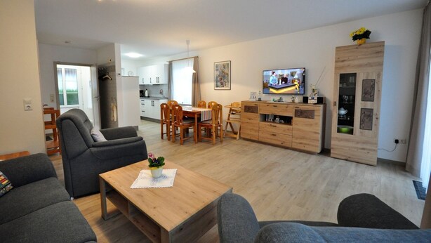 A modern living room with a wooden dining table, grey sofas, and a TV on a wooden cabinet. - Terraced house Am Haustierpark House 11 M - Am Haustierpark (Werdum)