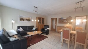 Uma sala de estar com sofá, poltronas, mesa de centro e um espaço de jantar com cadeiras e mesa.