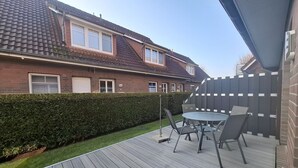 Um deck de madeira com mesa e cadeiras, um sebedo e uma casa ao fundo.