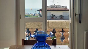 A blue vase on a table by a window with a view of a beach and a building labeled "FANATIKO". - Imperiale front beach Apartment  (Viareggio)