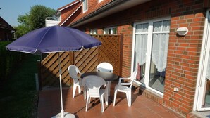 Eine Terrasse mit Tisch und Stühlen, einem blauen Sonnenschirm und einem Backsteinhaus mit Holzzaun.