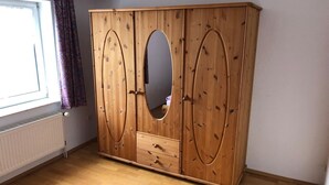 Ein Holzschrank mit zwei Türen und einem Spiegel in der Mitte, in einem Raum mit Heizkörper und Fenster.
