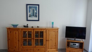 Eine Holzschrank mit Glastüren, ein Flachbildfernseher auf einem Standfuß und ein gerahmtes Bild an der Wand.