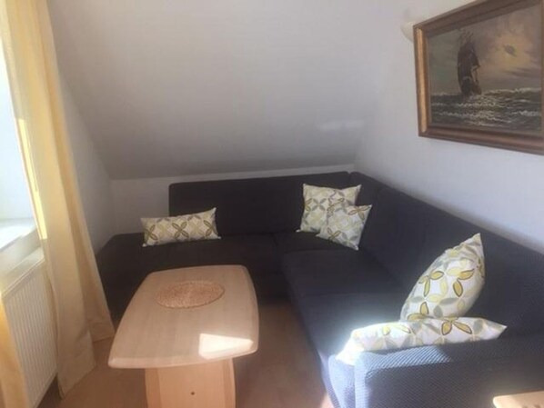 A corner room with a dark blue sofa, a small wooden table, and a painting on the wall.
