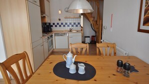 Cocina compacta con armarios de madera, lavavajillas y una mesa de comedor con tetera y saleros.