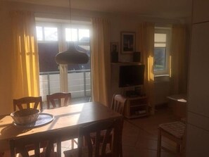 Un coin repas avec une table et des chaises, un téléviseur et une fenêtre avec des rideaux.