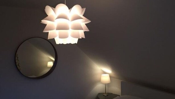 Un dormitorio con cama, lámpara de noche, espejo en la pared y una lámpara colgante.
