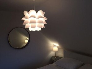 Un dormitorio con cama, lámpara de noche, espejo en la pared y una lámpara colgante.
