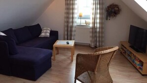 Una sala de estar acogedora con un sofá, un sillón de mimbre, una mesita y un mueble para televisión.