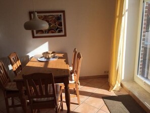 A dining area with a wooden table, chairs, a hanging light fixture, and a window with curtains.