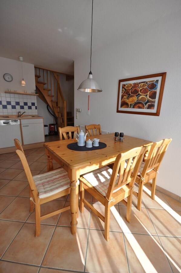 Un coin repas avec une table et des chaises en bois, un luminaire suspendu et une cuisine en arrière-plan.