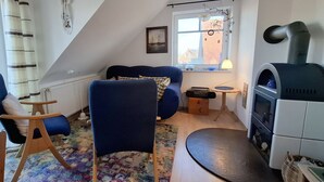 Une chambre à coucher confortable, aménagée en mezzanine, avec un plafond en pente, un canapé bleu, une petite table, une cheminée et une fenêtre donnant sur des immeubles.