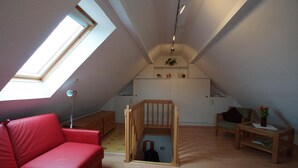 Une chambre à coucher aménagée dans un espace en hauteur, avec un plafond en pente, un canapé rouge, un espace de jeux en bois et un coin cuisine.