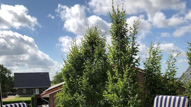 Une terrasse avec deux chaises à rayures et une petite table, un ciel dégagé et une maison en arrière-plan.