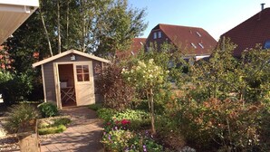 Ein Gartenweg führt zu einer kleinen Holzhütte mit Tür und Fenstern.