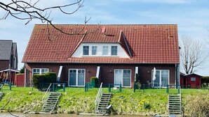 A two-story brick house with a red-tiled roof, a front porch, and a small garden.