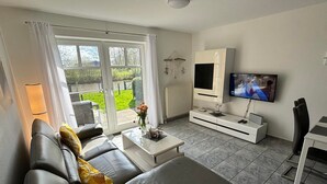 A modern living room with a sofa, coffee table, TV, and a view of the garden through large windows.