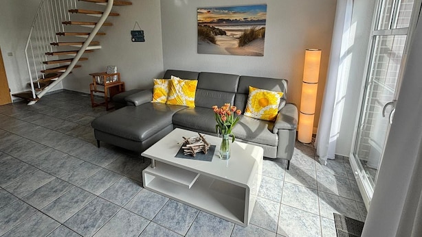 A modern living room with a grey sectional sofa, a white coffee table, a spiral staircase, and a large window.