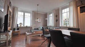 Ein modernes Wohnzimmer mit Essbereich, großen Fenstern und Deckenventilator.