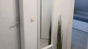 Un couloir avec une porte blanche, un miroir et une grande plante verte.