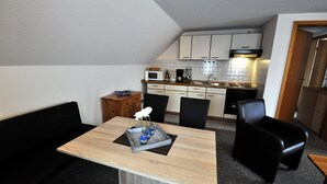 Une cuisine compacte avec des meubles blancs, un four à micro-ondes et une cuisinière. On y trouve également un coin repas avec une table en bois et des chaises noires.